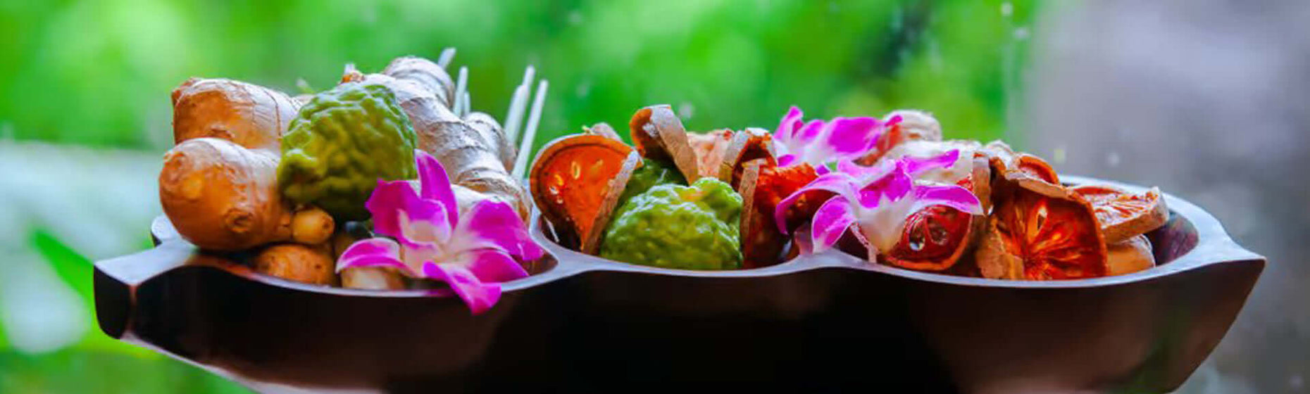 A bowl containing a variety of herbs, featuring turmeric, bilva, lemon, ginger, and other colorful ingredients.