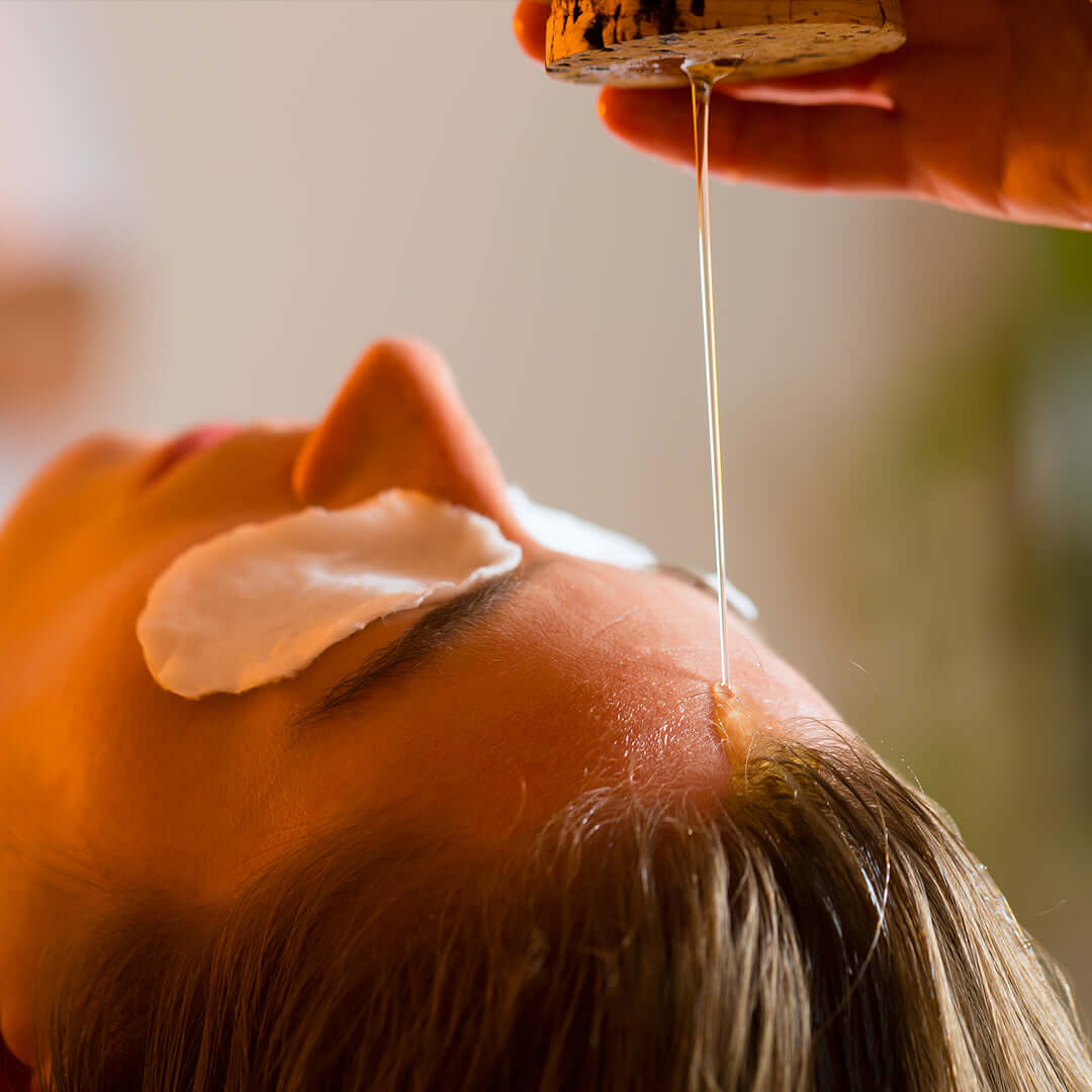 Oil therapy is performed on the forehead during an Ayurveda body detox to calm the mind, balance energy, and reduce stress.
